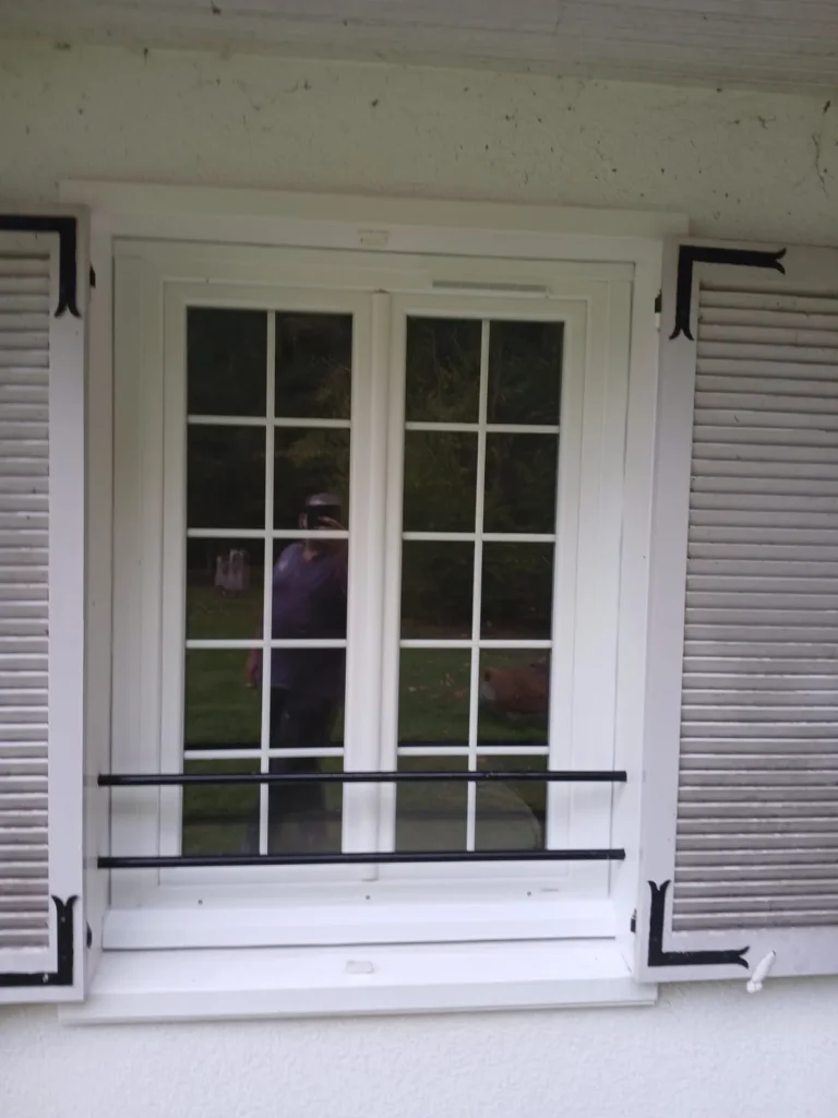 Fenêtre PVC blanche rénovée avec petits bois intégrés et volets battants gris ouverts, installée dans une maison du Val-de-Marne.